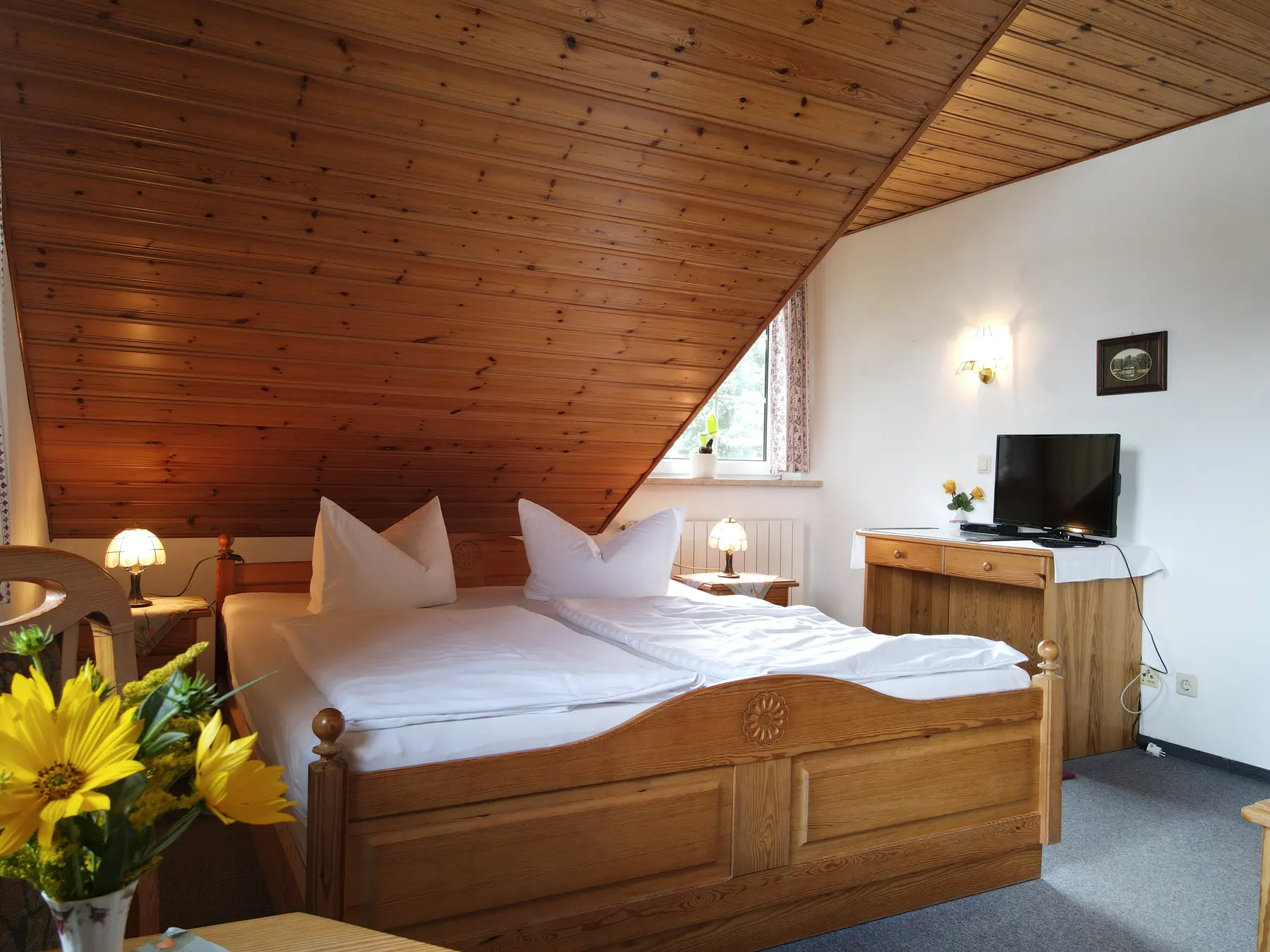 Helles Doppelzimmer mit warmem Holz und Blumen